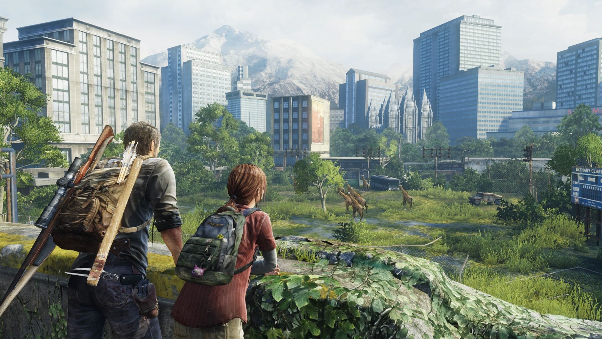 A post-apocalyptic scene from the video game "The Last of Us," featuring Joel and Ellie looking out over a overgrown cityscape towards a herd of giraffes in a park, with snow-capped mountains in the background. Joel carries a rifle and a backpack with arrows, while Ellie wears a backpack with accessories. Tall buildings are visible across a field of overgrown grass and a destroyed vehicle.