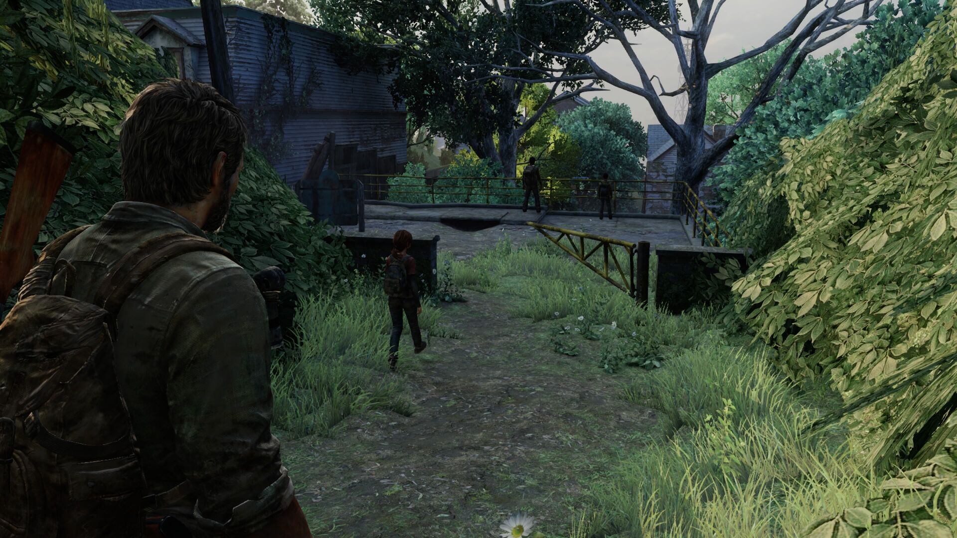 In a post-apocalyptic setting, a man with a backpack and a shotgun observes a young girl walking towards a bridge guarded by two figures. Overgrown vegetation surrounds the area, with abandoned houses in the background.