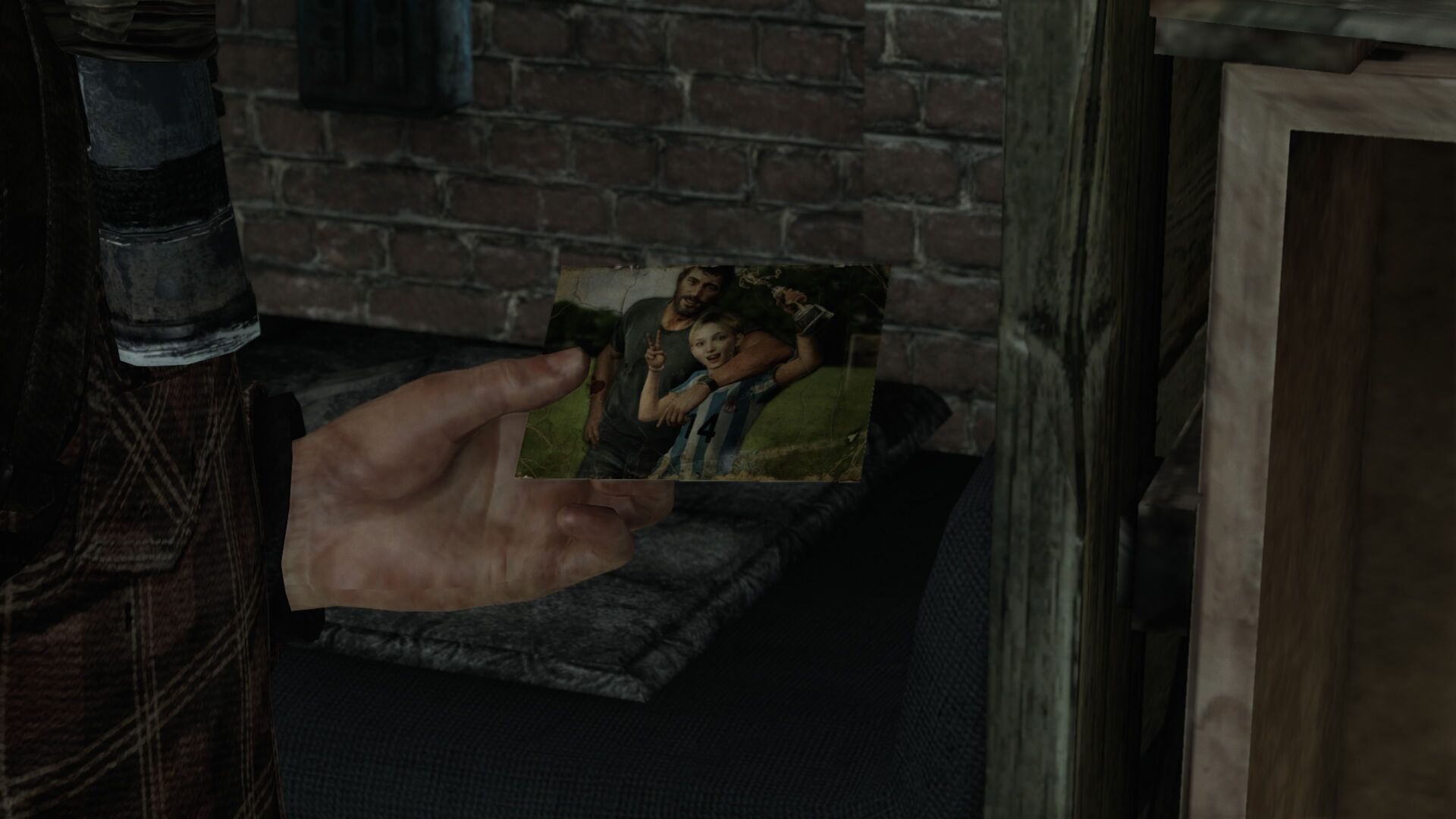 A worn photograph held by a person depicting a man with a beard and a young girl embracing on a grassy field, with the girl holding a trophy, the man giving the peace sign.